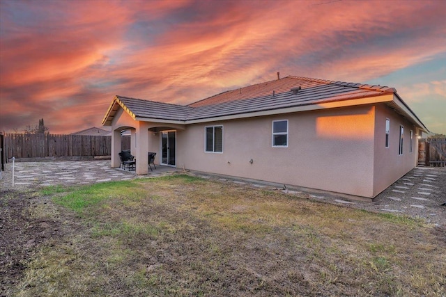 back house at dusk with a patio area and a lawn