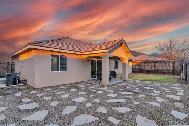 back house at dusk with central AC and a patio area