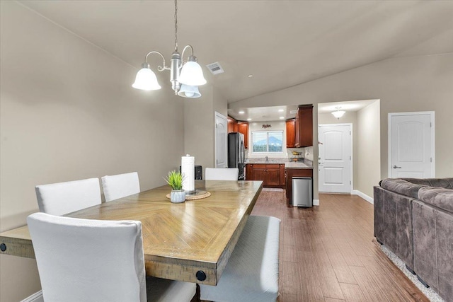 dining room with lofted ceiling, dark wood-type flooring, sink, and a chandelier