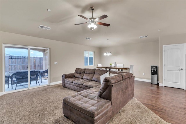 living room with ceiling fan with notable chandelier and dark hardwood / wood-style flooring