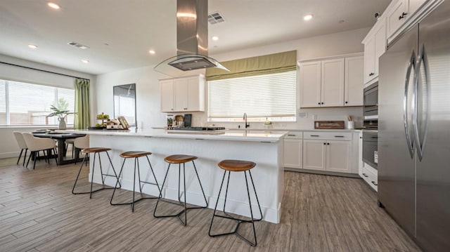 kitchen featuring appliances with stainless steel finishes, white cabinets, a breakfast bar, and island range hood