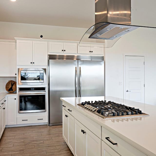 kitchen with white cabinetry, island exhaust hood, and built in appliances