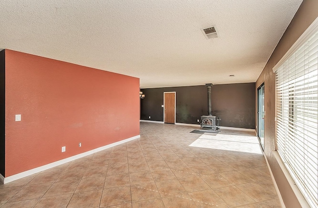 empty room featuring light tile patterned floors, a textured ceiling, and a wood stove