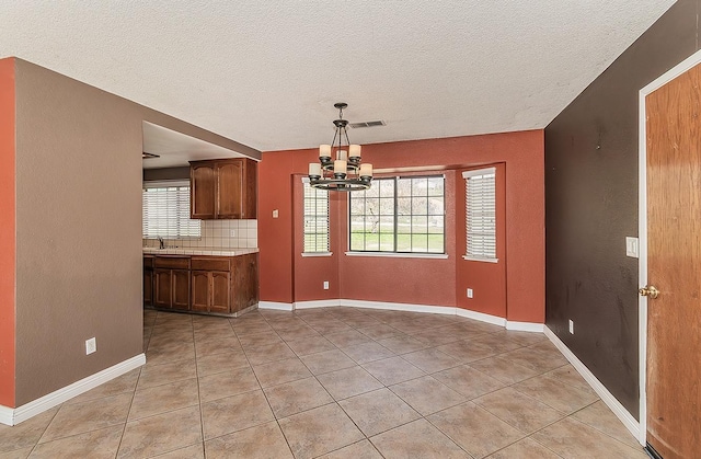 unfurnished dining area featuring light tile patterned floors, a textured ceiling, and a chandelier