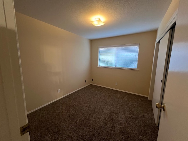 unfurnished bedroom featuring a textured ceiling, dark carpet, and a closet