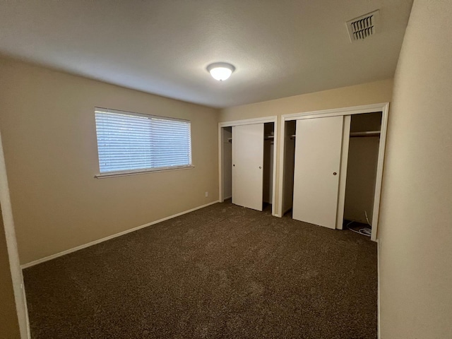 unfurnished bedroom featuring dark colored carpet and two closets