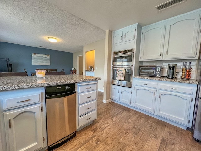 kitchen featuring white cabinetry, stainless steel appliances, light stone countertops, light hardwood / wood-style floors, and a textured ceiling