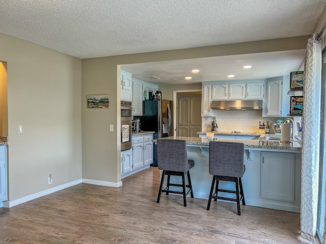 kitchen featuring a breakfast bar, kitchen peninsula, sink, light hardwood / wood-style floors, and stainless steel fridge with ice dispenser