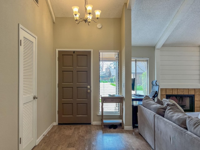 entryway featuring an inviting chandelier, a textured ceiling, a fireplace, and wood-type flooring