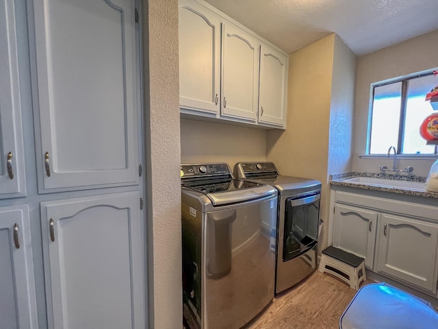 clothes washing area featuring cabinets, sink, independent washer and dryer, and light hardwood / wood-style flooring