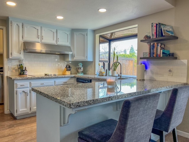 kitchen with sink, white cabinets, kitchen peninsula, light stone countertops, and light hardwood / wood-style flooring