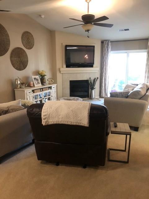 carpeted living room with ceiling fan, lofted ceiling, and a fireplace