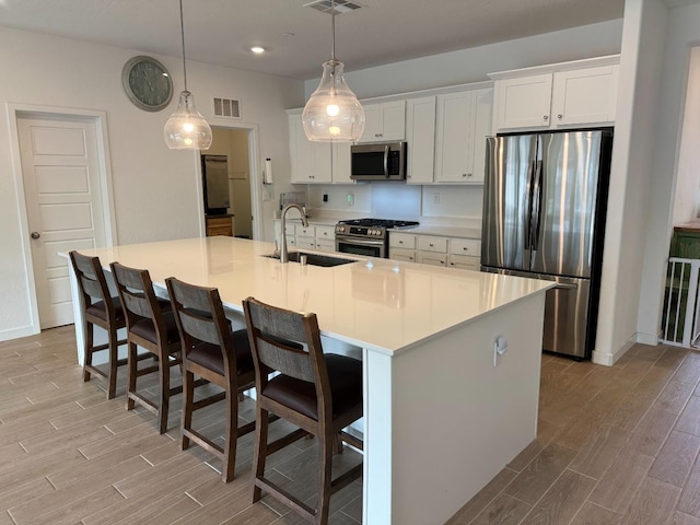 kitchen with sink, white cabinetry, pendant lighting, stainless steel appliances, and a kitchen island with sink