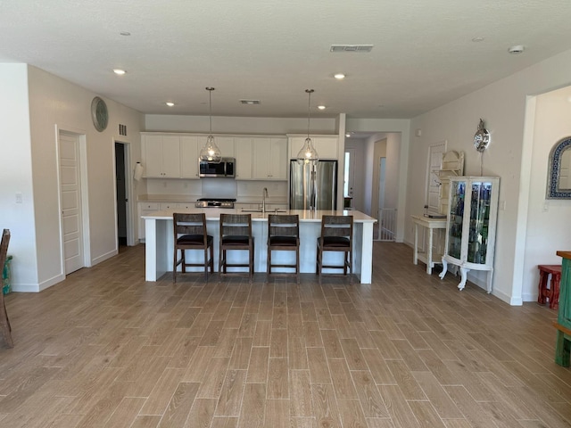 kitchen featuring a spacious island, hanging light fixtures, a kitchen breakfast bar, stainless steel appliances, and white cabinets