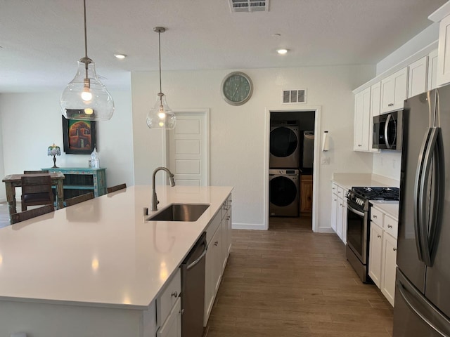 kitchen with sink, stacked washing maching and dryer, a kitchen island with sink, white cabinetry, and stainless steel appliances