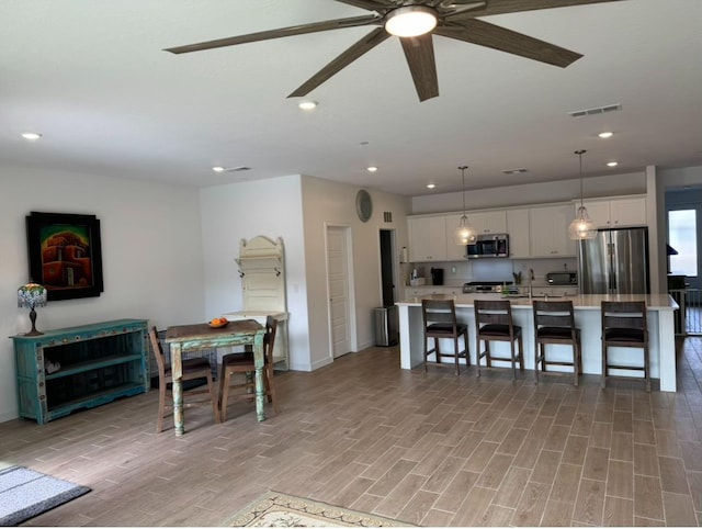 dining room featuring sink, a breakfast bar area, white cabinetry, an island with sink, and pendant lighting