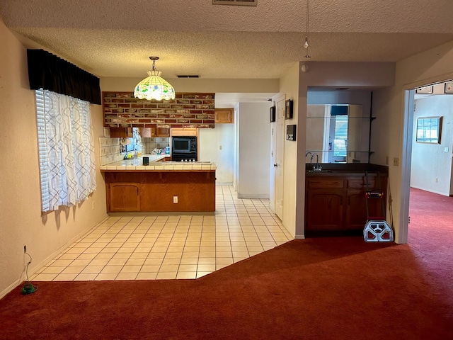 kitchen featuring tile countertops, pendant lighting, kitchen peninsula, light carpet, and a textured ceiling