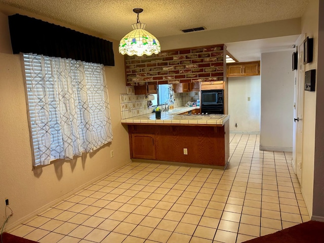 kitchen with tile countertops, kitchen peninsula, decorative light fixtures, black appliances, and a healthy amount of sunlight