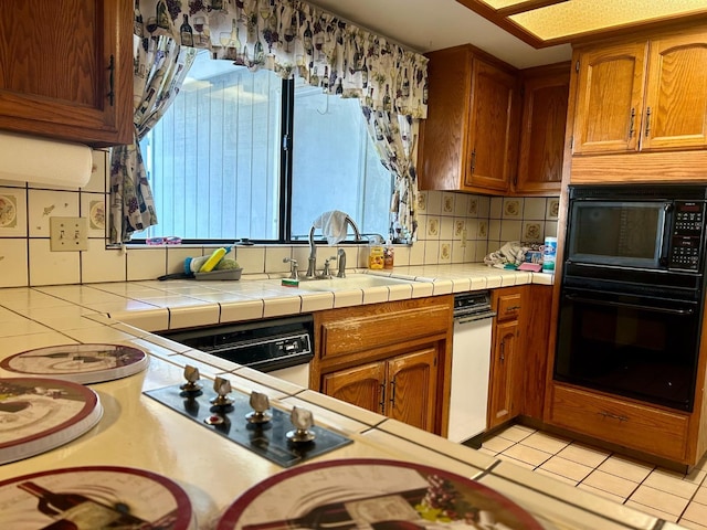 kitchen featuring sink, light tile patterned floors, backsplash, tile counters, and black appliances