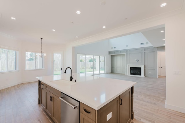 kitchen with sink, crown molding, a center island with sink, stainless steel dishwasher, and light wood-type flooring