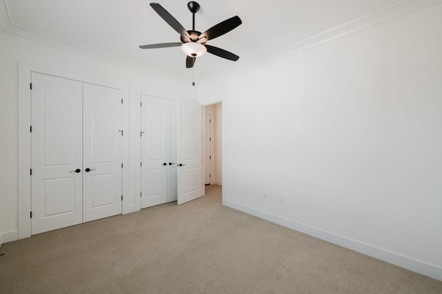 unfurnished bedroom featuring light carpet, ceiling fan, ornamental molding, and multiple closets