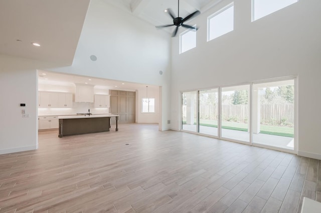 unfurnished living room featuring beamed ceiling, sink, ceiling fan, and light hardwood / wood-style flooring