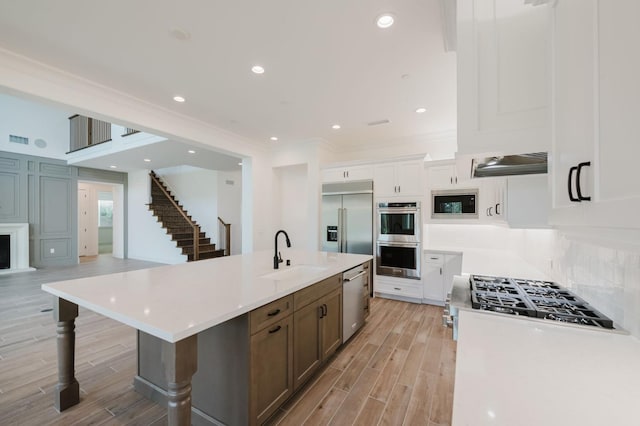 kitchen with sink, white cabinets, backsplash, built in appliances, and a spacious island