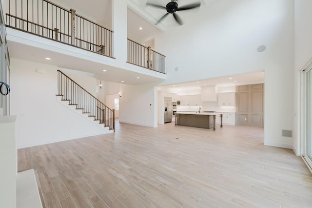 unfurnished living room with ceiling fan, light hardwood / wood-style flooring, and a towering ceiling