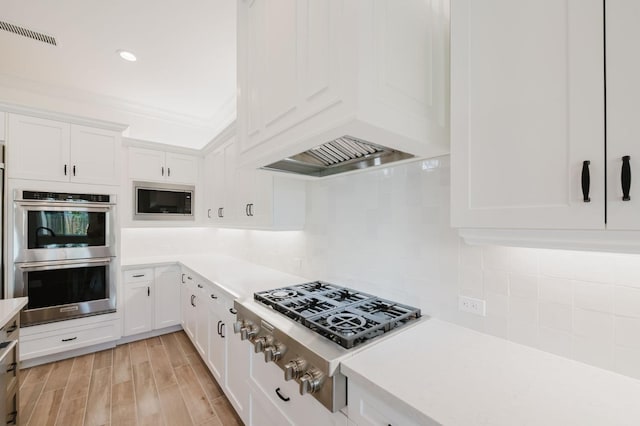 kitchen featuring appliances with stainless steel finishes, tasteful backsplash, white cabinetry, custom range hood, and light wood-type flooring