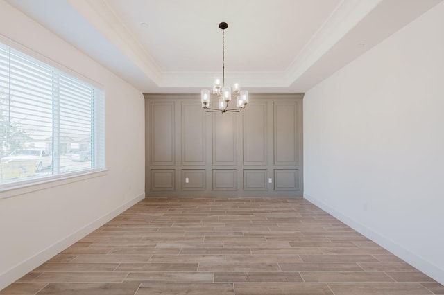 unfurnished dining area featuring ornamental molding, a notable chandelier, and a tray ceiling