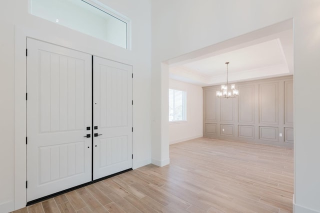 foyer featuring light hardwood / wood-style flooring, a chandelier, and a tray ceiling