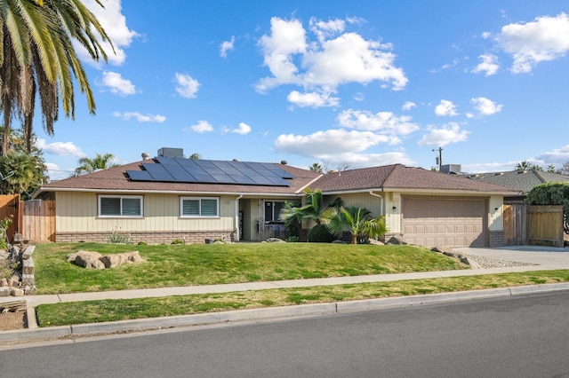 ranch-style home with driveway, solar panels, a garage, fence, and a front lawn