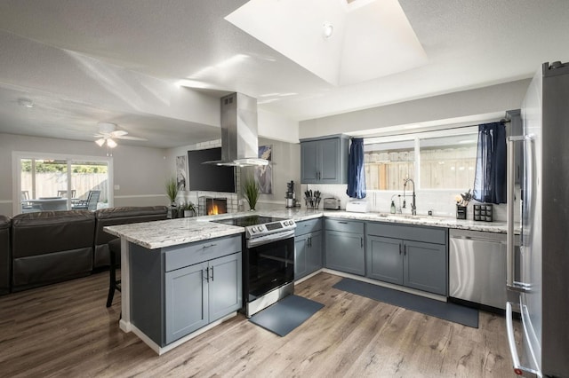 kitchen featuring appliances with stainless steel finishes, a sink, gray cabinets, a peninsula, and island exhaust hood
