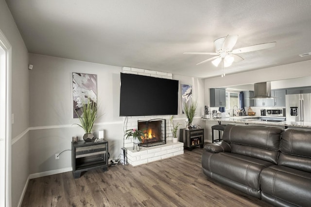 living room with baseboards, a ceiling fan, a brick fireplace, and wood finished floors