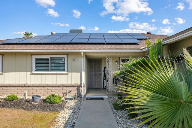 view of exterior entry featuring a shingled roof, solar panels, and brick siding