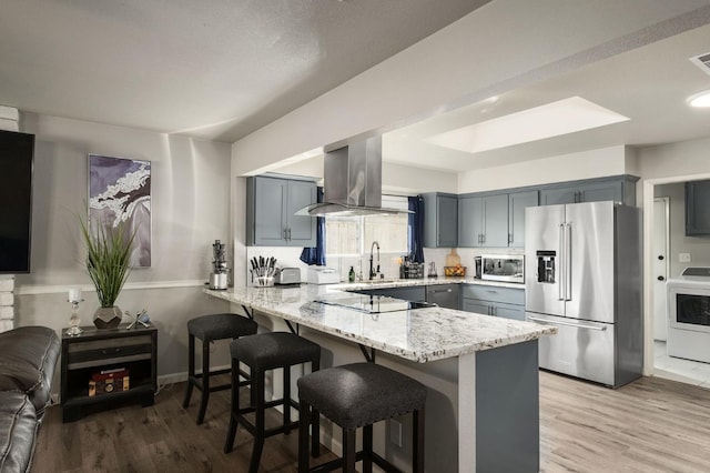 kitchen featuring a kitchen breakfast bar, island exhaust hood, appliances with stainless steel finishes, light stone counters, and a peninsula