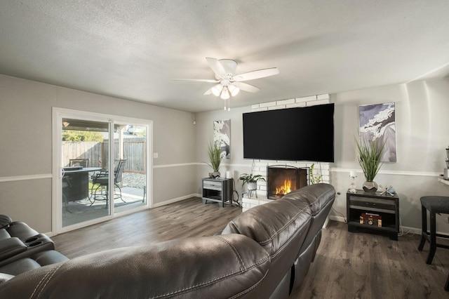 living room with baseboards, ceiling fan, a stone fireplace, and wood finished floors