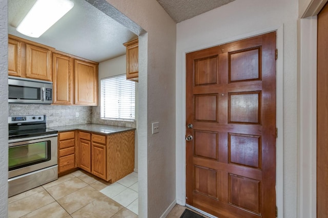 kitchen with stainless steel appliances, tasteful backsplash, light tile patterned floors, and a textured ceiling