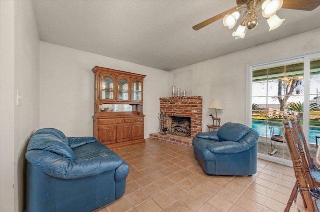 living room featuring ceiling fan, a fireplace, a textured ceiling, and light tile patterned floors