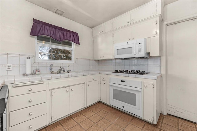 kitchen with white cabinetry, white appliances, tile counters, and tasteful backsplash