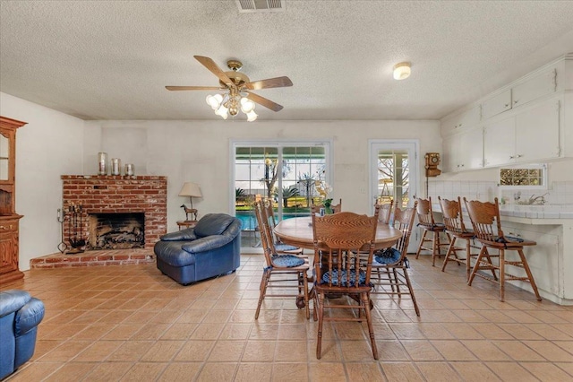 tiled dining space with a textured ceiling, a fireplace, and ceiling fan