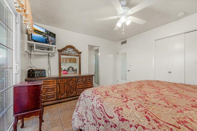 bedroom with tile patterned flooring, ceiling fan, a closet, and a textured ceiling