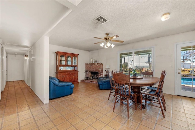 dining space featuring a brick fireplace, a textured ceiling, and ceiling fan