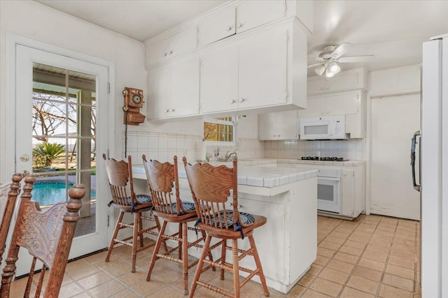 kitchen featuring white cabinetry, a breakfast bar area, tile countertops, and white appliances