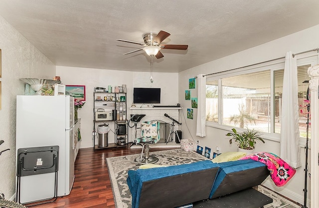 living room featuring dark hardwood / wood-style flooring, ceiling fan, and a textured ceiling