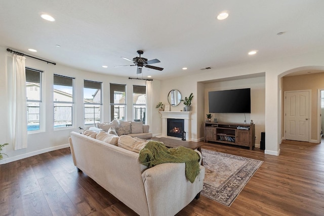 living room featuring dark wood-type flooring, ceiling fan, and a wealth of natural light