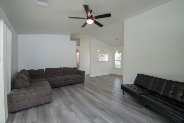 living room featuring light wood finished floors, visible vents, arched walkways, vaulted ceiling, and a ceiling fan