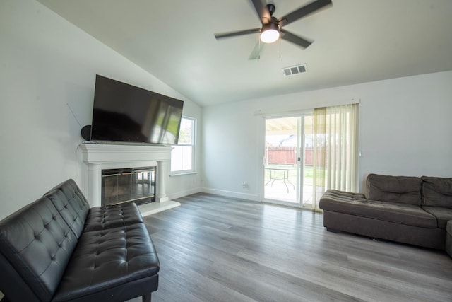 living area with visible vents, a ceiling fan, light wood finished floors, vaulted ceiling, and a glass covered fireplace