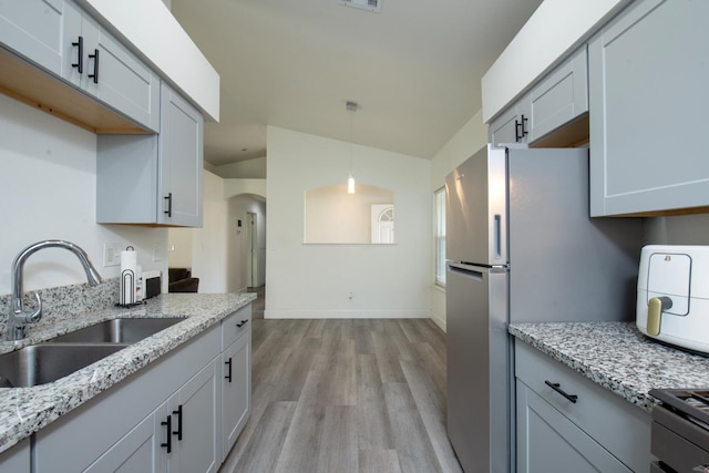 kitchen featuring a sink, light stone counters, pendant lighting, baseboards, and light wood-style floors