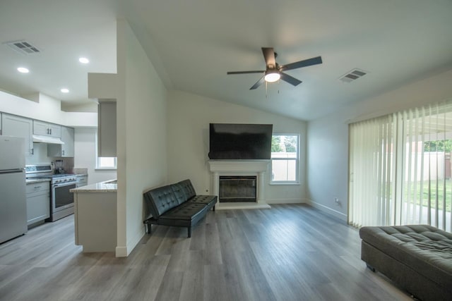 living area featuring a glass covered fireplace, visible vents, lofted ceiling, and light wood-type flooring